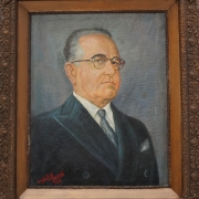 Quadro emoldurado sobre cavalete de madeira com o retrato de Get&iacute;lio Vargas, de terno escuro e &oacute;culos