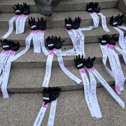 Esculturas de mãos feitas em gesso de cor preta posicionadas nos degraus de uma escadaria, com fitas de papel citando nomes de mulheres e frases de combate ao feminicídio